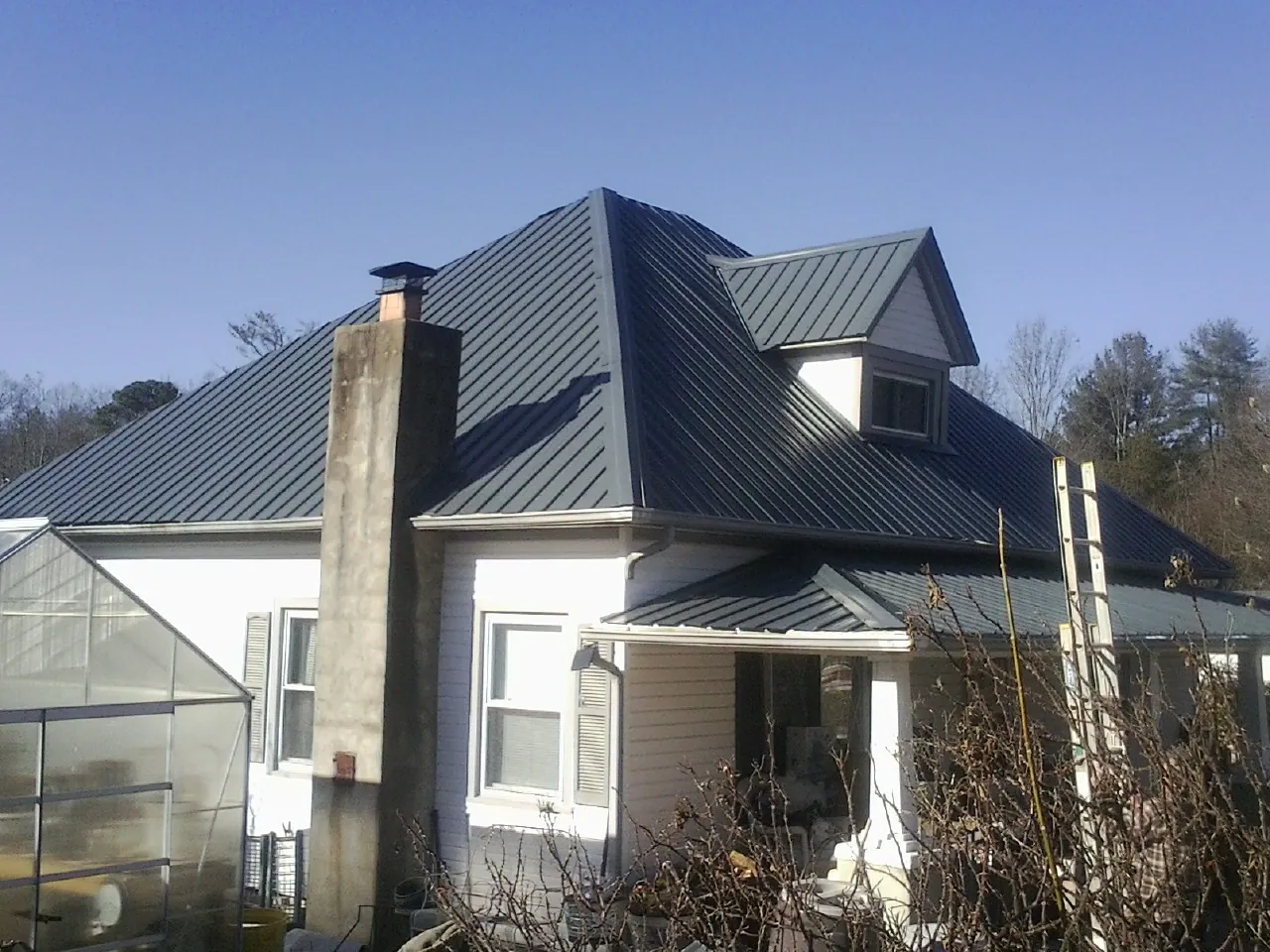 Dark blue standing seam metal roof on a white farmhouse with dormer — Slate & Tile Roof Repair by Roofing Brothers in Bracey