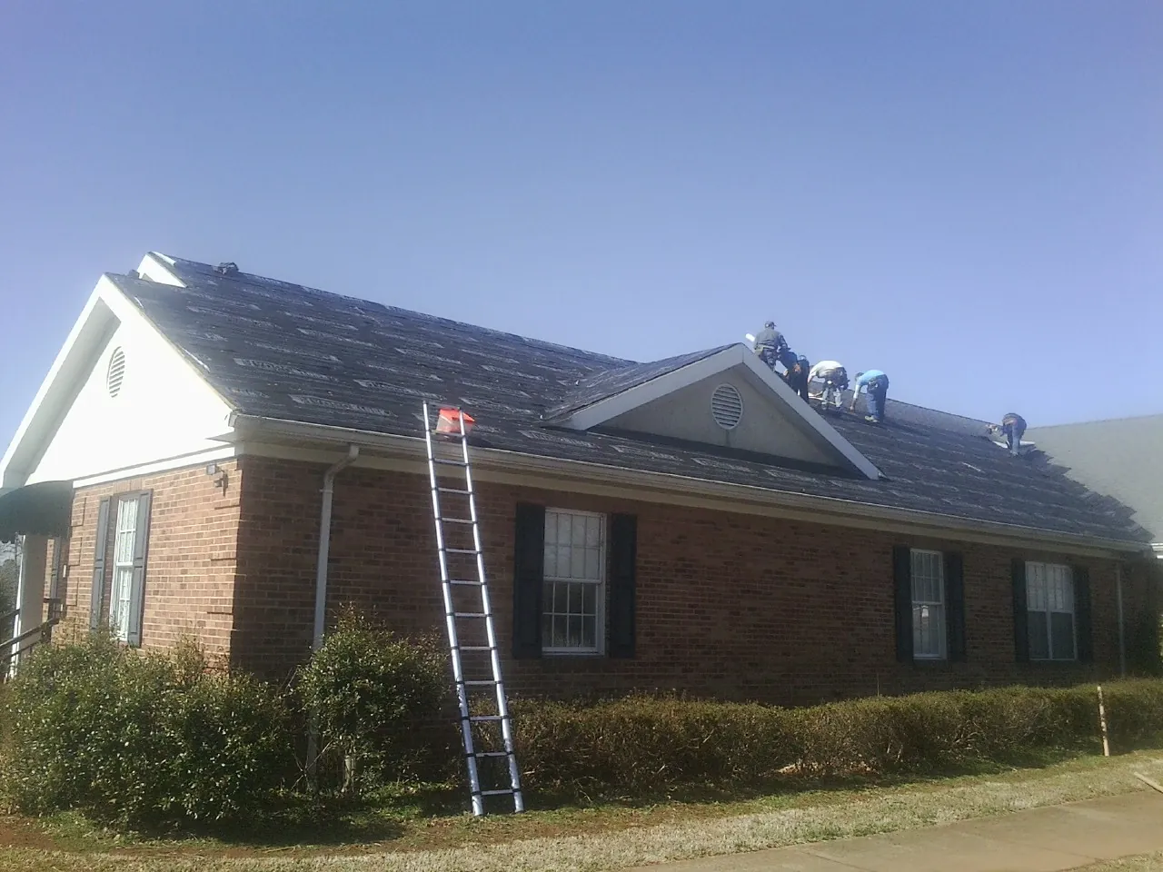 Crew tearing shingles off a brick ranch roof with a ladder set — Metal Roof Repair work by our crew in Bracey