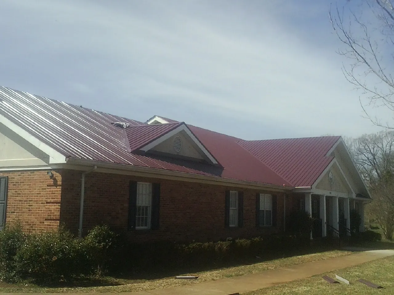Red metal roof with gabled entries on a long brick building, from a Hail Damage Roof Repair job in Bracey