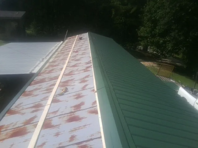 Old rusted panels beside newly installed green metal roofing — Wind Damage Roof Repair by Roofing Brothers in Bracey