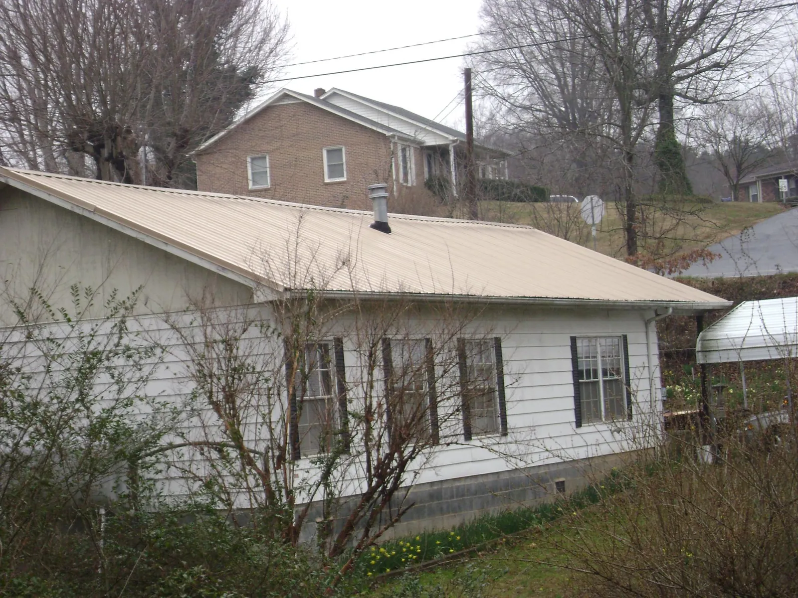 Tan metal roof on a white sided house set into a hillside — Commercial Roofing by Roofing Brothers in Bracey